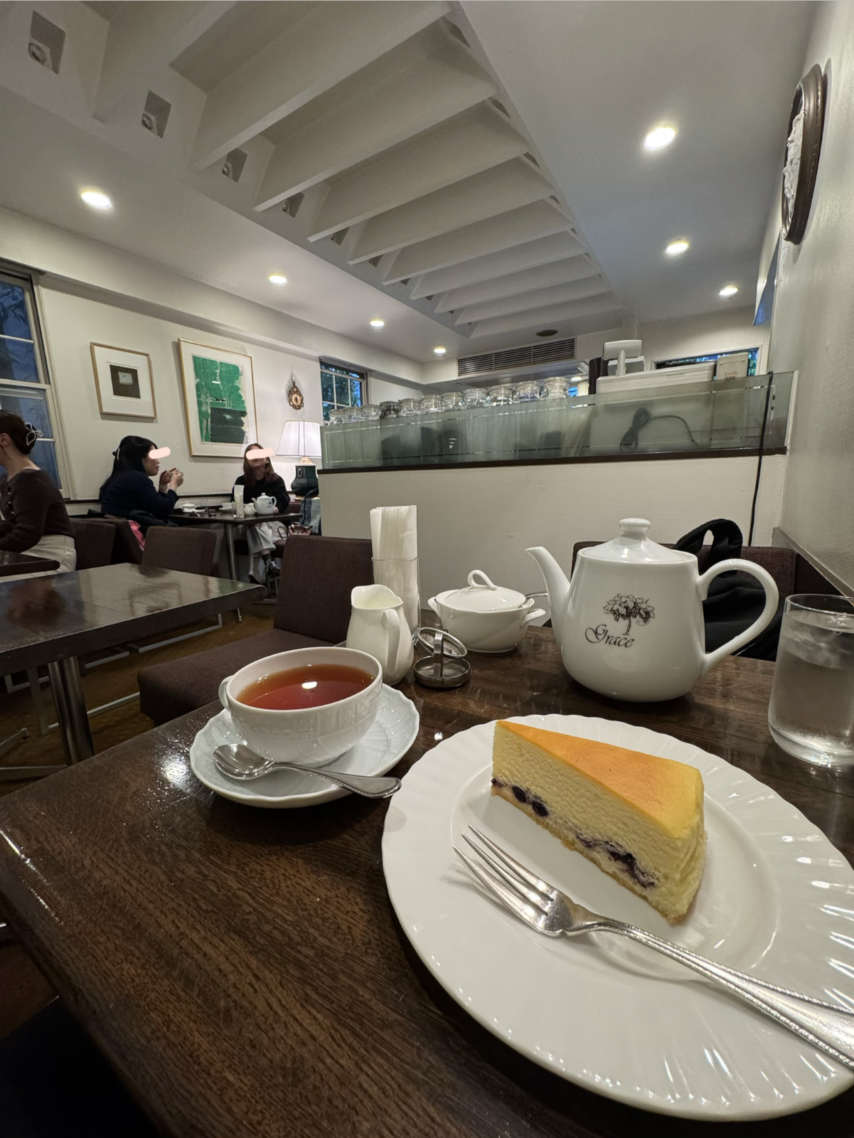 店内の窓辺と客席。奥のガラス棚には紅茶器具が並び、壁にはアートワークが掛けられている。
