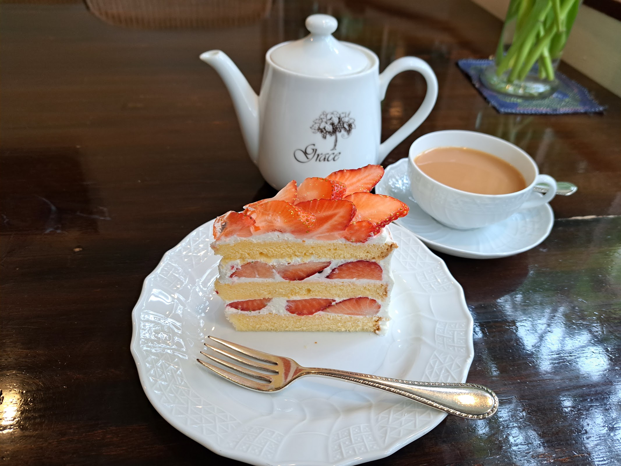 Grace 印の白い紅茶ポットと、いちごのショートケーキ。窓辺のテーブルで撮影。